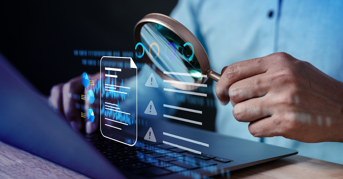 Person on laptop holding magnifying glass over alert data